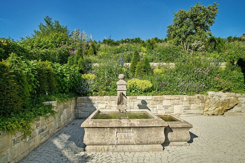 Ein antiker Brunnen inmitten eines romantischen Gartens mit üppigen Staudenpflanzen ist der optimale Platz für eine kleine Auszeit vom ­Alltag. Gartencenter Hoffmann AG, www.gartencenter-hoffmann.ch