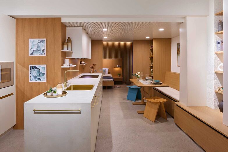 Einrichtung für ein Tiny House: Küche, Essplatz, Stauraum, Schlafzimmer und Bad finden auf kleinstem Raum Platz und bieten ein luftiges und funktionales Ambiente. Die Küche besticht durch einen hellen, warmen Farbton und harmoniert mit der fast gleichfarbigen Keramikabdeckung. Die Griffe, die Mischer und das Becken in zartem Gold sowie die Einbaugeräte und der Weinkühler in der Farbe Pearl verleihen einen Hauch von Luxus. Das Holzfurnier für Wände und Schiebetüre kann in der Produktion und Ausstellung in Wyssachen besichtigt werden. Die zweite Ausstellung befindet sich in Langenthal. 

Loosli AG, www.loosli.swiss